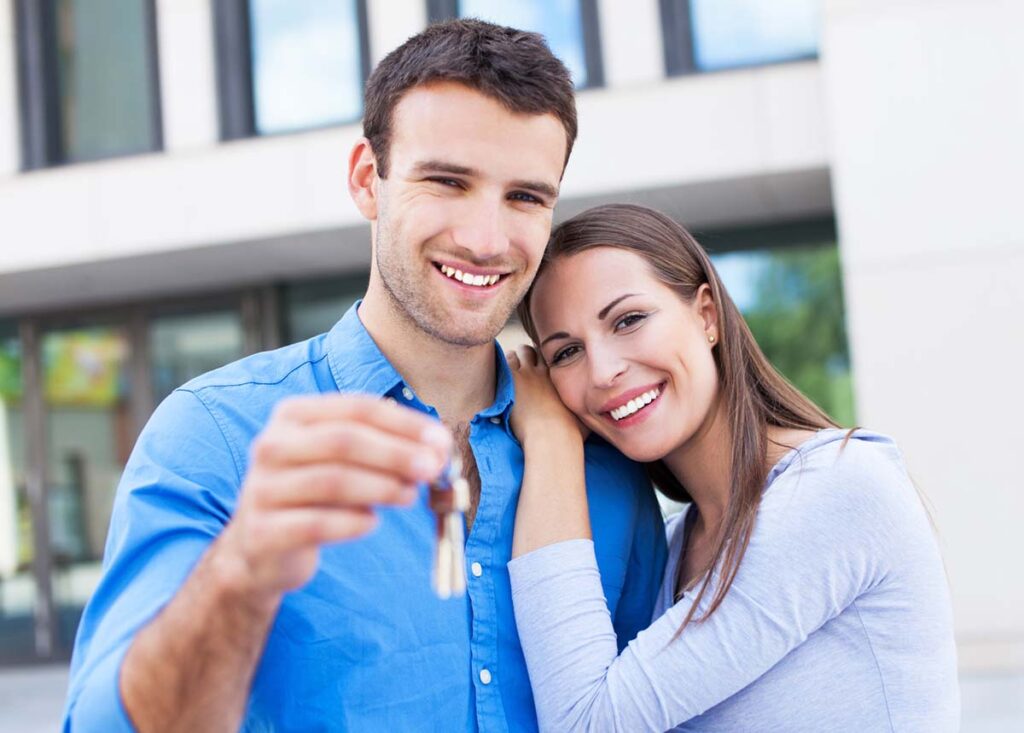 Nuevos propietarios de vivienda sosteniendo llaves frente a su casa