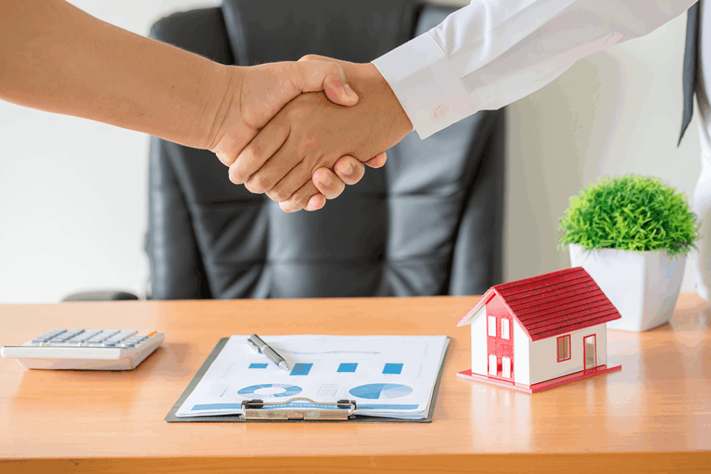 Agente inmobiliario y cliente dándose la mano tras firmar contrato de compra de apartamento
